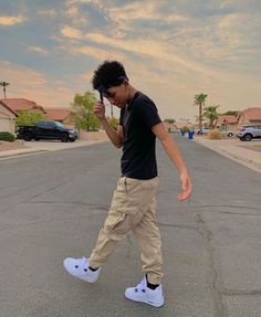 a young man is walking down the street with his cell phone to his ear while wearing white sneakers