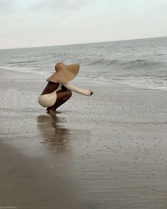 a woman kneeling on top of a beach next to the ocean