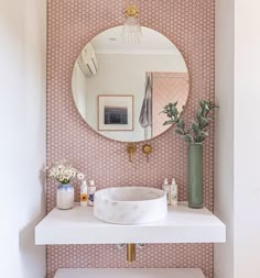 a white sink sitting under a round mirror next to a wall mounted faucet