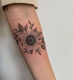 a woman's arm with a sunflower and leaves tattoo on the left forearm