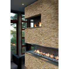 a modern fireplace in the middle of a living room with large windows and stone walls