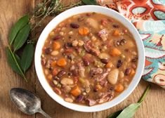 a white bowl filled with beans and carrots next to a spoon on top of a wooden table