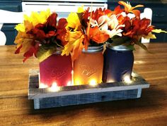 three mason jars with candles and flowers in them on a wooden tray that is sitting on a table