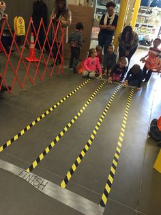 children are sitting on the floor in front of yellow caution tape as adults look on