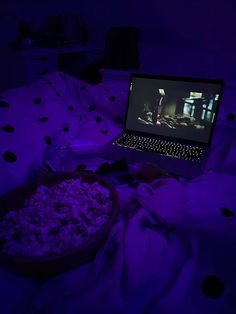 a laptop computer sitting on top of a bed next to a bowl filled with popcorn