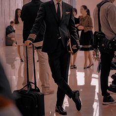 a man in a suit and tie pulling luggage through an airport terminal with other people