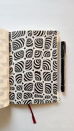 an open notebook with black and white designs on it, next to a fountain pen