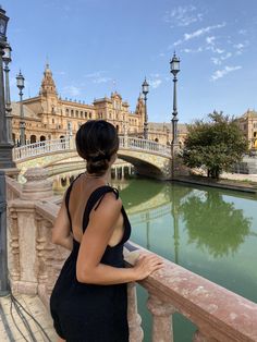 a woman standing on a bridge looking at the water in front of a building and lampposts