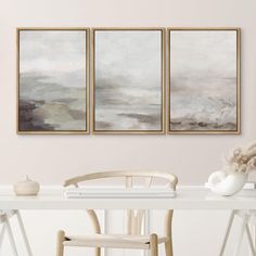 three paintings hang on the wall above a white table with two chairs and a vase