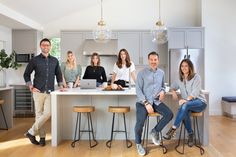 a group of people sitting at a kitchen counter with laptops on the island in front of them