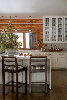 a kitchen with white cabinets and wooden floors, two chairs at the center of the island