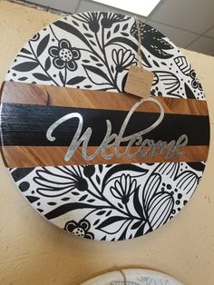 a wooden sign that says welcome hanging on the wall next to two plates with flowers