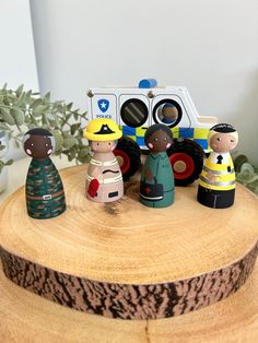 three wooden toy figures on top of a tree stump with a fire truck in the background