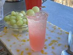 a glass filled with fruit sitting on top of a table next to a bowl of grapes