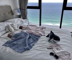 two babys laying on a bed next to each other with the ocean in the background