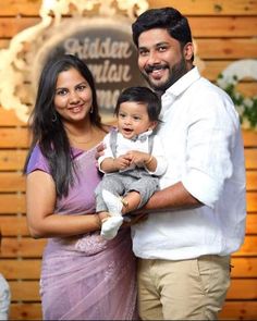 a man and woman holding a baby in front of a wooden wall