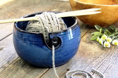 yarn and knitting needles in a blue bowl on a wooden table next to a wood bowl