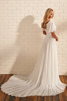 a woman standing in front of a brick wall wearing a white dress