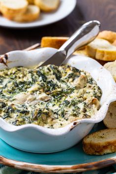 spinach dip in a white bowl on a blue plate with crackers and bread