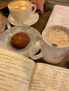 there is a cup of coffee and a muffin on the table next to an open book