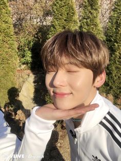 a man with his hand on his chin looking up at the sky and trees behind him