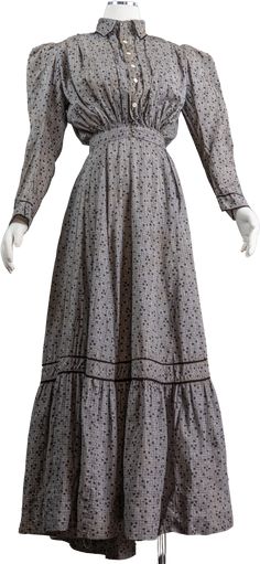 This is a gorgeous 1890s cotton calico wrap dress. The dress is printed with adorable black shamrocks and white dots and is on a gray checked base. The dress has a high collared neckline and buttons down the front with a puffy almost pigeon-breasted style top. It has large puffy leg of mutton sleeves that are looser for the more casual wear of this dress. The dress is fitted at the waist with a waistband that has two hooks and eyes that keep the dress closed. The skirt wraps to the left to fasten with a hook to the waistband and then there is a slit in the skirt that can be used to access a tie-on pocket if you would like. The slit is well hidden and does not open. The skirt of the dress is a wonderful full A-line with a flounce at the hem. At the center back of the skirt the dress has box 1880s Dresses Casual, Early Victorian Dress, Late Victorian Dress, 1890s Dress Poor, Victorian Winter Dress, Victorian Wrapper Dress, Victorian Summer Dress, 1880s Day Dress, Plus Size Victorian