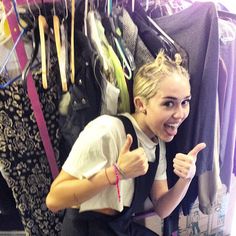 a woman sitting in front of a rack of clothes and giving the thumbs up sign