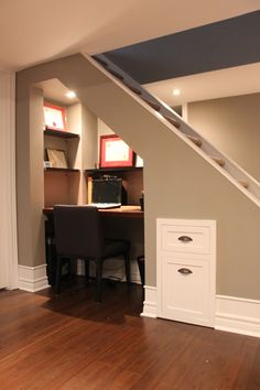 an empty room with a desk and chair under the stairs