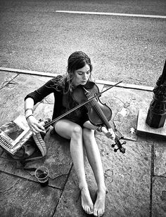 a woman sitting on the ground playing a violin with her feet propped up in front of her