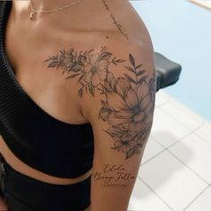 a woman wearing a black top with flowers on her arm and shoulder, in front of a tiled wall