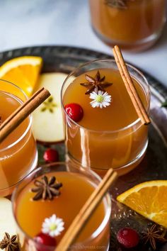 two glasses filled with orange juice and cinnamon sticks on top of an oval tray next to sliced apples