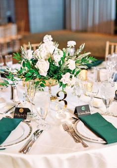 the table is set with white flowers and green napkins, silverware and place settings