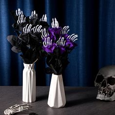 two white vases with purple flowers in them on a table next to a skeleton