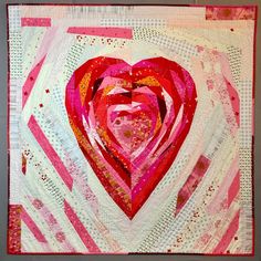 a quilted heart is displayed on the wall in front of a gray background with pink and white stripes