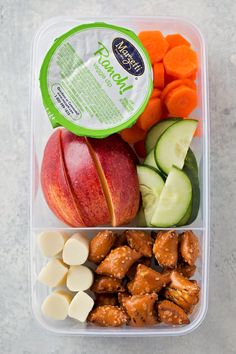 a plastic container filled with different types of vegetables and meats next to sliced apples, cucumbers, and carrots