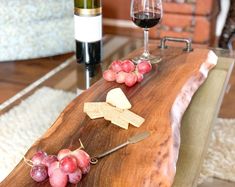 a wooden table topped with grapes and cheese next to a bottle of wine on top of a rug