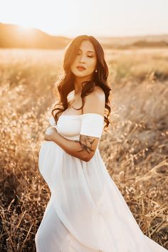 a pregnant woman in a white dress standing in tall grass with her hands on her stomach