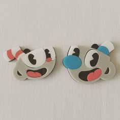 two pieces of cartoon character brooches on a white cloth covered surface with red, blue and black eyes