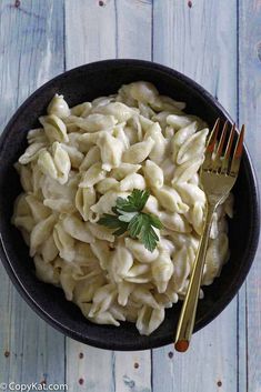 a black bowl filled with pasta and garnished with parsley next to a fork