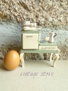 an egg sitting on a table next to a miniature stove and toaster with the words vintage stove written below it