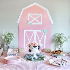 a table topped with plates and cakes next to a pink barn