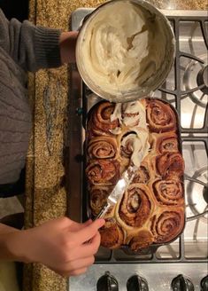 a person is spreading icing on top of a cinnamon roll in the oven with a spatula