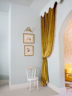 a white chair sitting in front of a window next to a wall with pictures on it