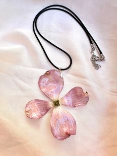 a pink flower is attached to a black cord on a white sheet with a silver clasp