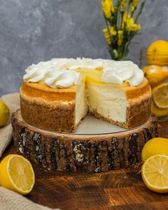 a cheesecake with lemons around it on a wooden table next to some flowers