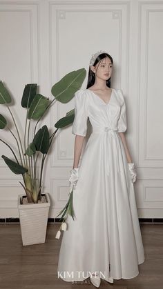 a woman in a white dress standing next to a potted plant