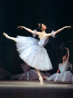 two ballerinas in white tutus and blue dresses, one with her arms outstretched