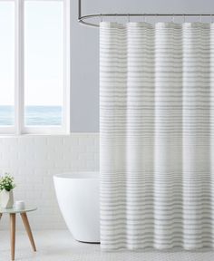 a white shower curtain in a bathroom next to a bathtub and table with flowers on it