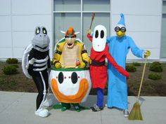 three people in costumes are standing on the sidewalk and posing for a photo while one person is holding a broom