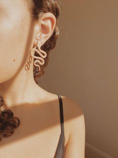 a woman with large earrings on her neck looking off into the distance while standing in front of a wall